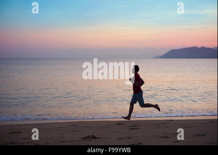 Young man running on the beach at sunset Stock Photo