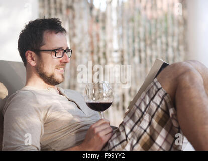 Young handsome man relaxing, reading book and drinking red wine Stock Photo
