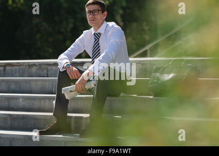 Well dressed business man reading newspaper sitting on a street sidewalk Stock Photo