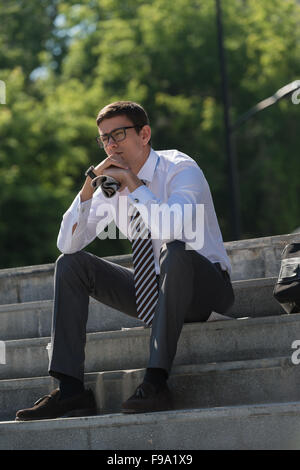 Young businessman resting in sunlight on stairs outdoors and thinking Stock Photo