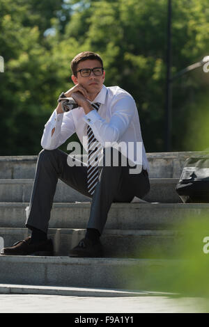 Young businessman resting in sunlight on stairs outdoors and thinking Stock Photo