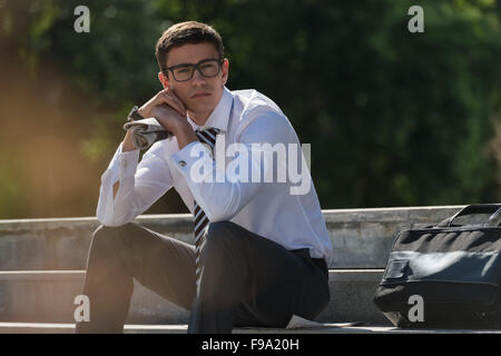 Young businessman resting in sunlight on stairs outdoors and thinking Stock Photo