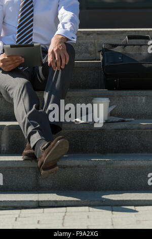 Young man drinking coffee outdoors at park and using tablet computer Stock Photo