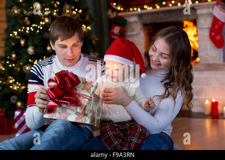 Happy family opening Christmas gift sitting in decorated living room Stock Photo