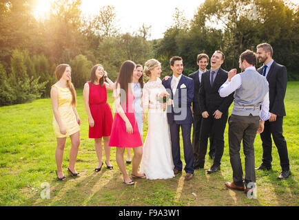 Full length portrait of newlywed couple having fun with bridesmaids and groomsmen in green sunny park Stock Photo