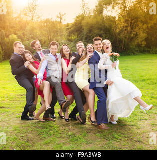 Full length portrait of newlywed couple having fun with bridesmaids and groomsmen in green sunny park Stock Photo