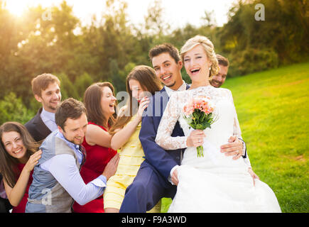 Portrait of newlywed couple having fun with bridesmaids and groomsmen in green sunny park Stock Photo