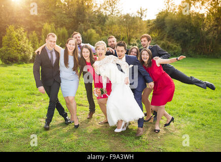 Full length portrait of newlywed couple having fun with bridesmaids and groomsmen in green sunny park Stock Photo