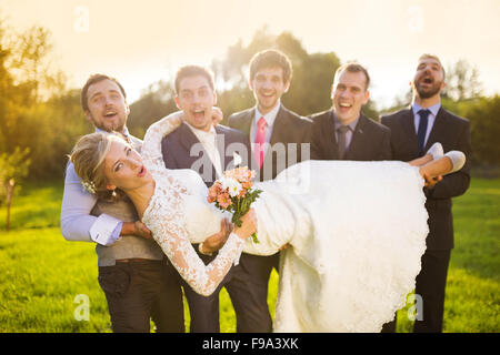 Outdoor portrait of young groom with his friends holding beautiful bride Stock Photo