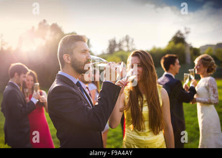 Wedding guests drinking champagne while the newlyweds clinking glasses in the background Stock Photo