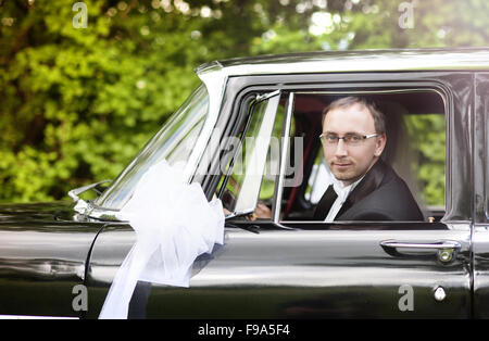 Happy young groom looking out of the retro car Stock Photo