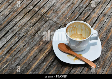 One overdrunk finished white cup of espresso coffee on porcelain saucer with wooden spoon on old vintage bamboo table Stock Photo