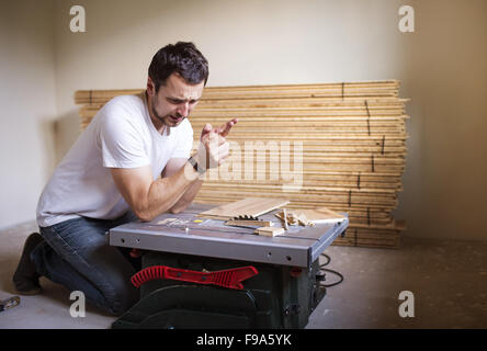 Young handyman having accident during cutting plywood on circular saw Stock Photo