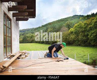 Handyman installing wooden flooring in patio, working with drilling machine Stock Photo