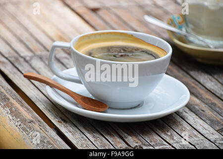 One full white cup of Americano long coffee on porcelain saucer with wooden spoon on old vintage bamboo table Stock Photo