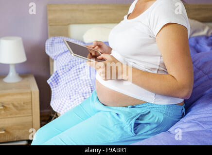 Unrecognizable pregnant woman using digital tablet in her bedroom Stock Photo