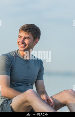 Sporty man resting after workout on beach during sunset