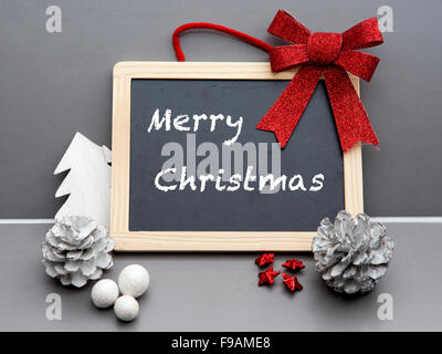 'Merry Christmas' written on blackboard with red ribbon and pine cones Stock Photo