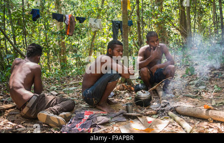 Three young aboriginal Orang Asil men sitting on the ground in the jungle, smoking, indigenous culture, tropical rainforest Stock Photo