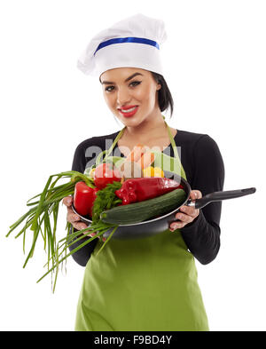 Beautiful young hispanic cook holding many vegetables in a frying pan Stock Photo