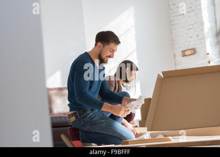 Happy young couple putting together self assembly furniture as they move into their new house. Stock Photo