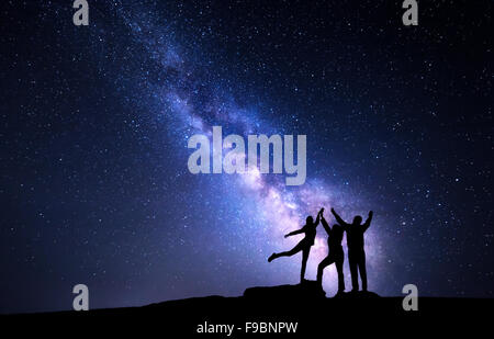 Milky Way. Night sky with stars and silhouette of a happy family with raised-up arms Stock Photo