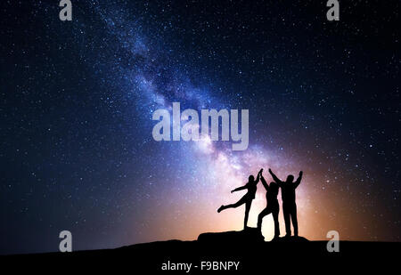 Milky Way. Night sky with stars and silhouette of a happy family with raised-up arms Stock Photo