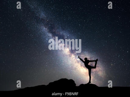 Milky Way. Night sky with stars and silhouette of a woman practicing yoga. Stock Photo