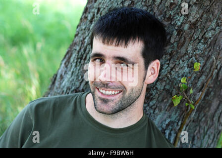 Young man leaning on tree is looking at camera. Stock Photo