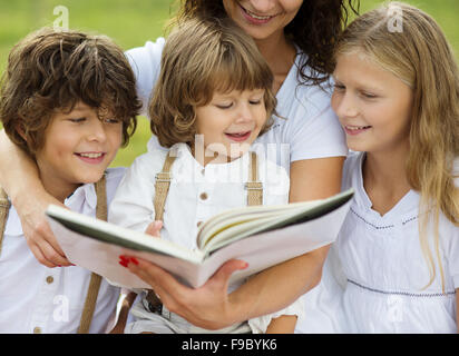 Mother is seating and reading a book to her children in the green park Stock Photo