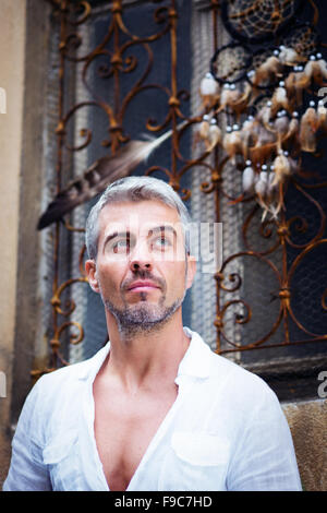 Sexi Man in a white shirt and ornamental window on background. And Dream Catcher a eagle feather. Stock Photo