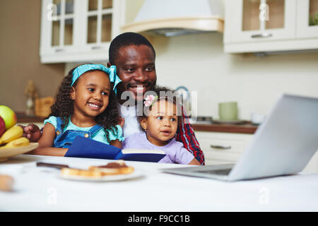 Happy young man with two daughters watching cartoons in the kitchen Stock Photo