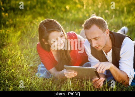 Happy couple is lying on the grass and playing with tablet Stock Photo