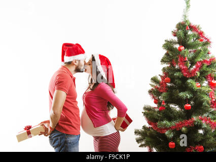 Young couple is dancing close to christmas tree. Woman is pregnant.