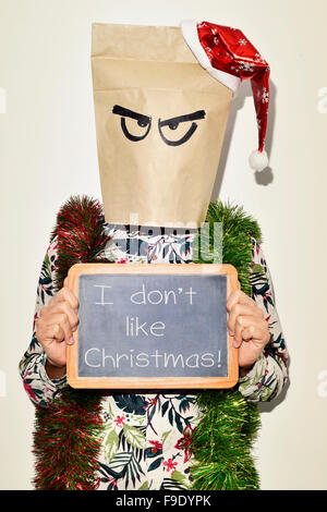 a young man dressing casual wear with a paper bag in his head and a santa hat in the top and some tinsel in his shoulders shows Stock Photo