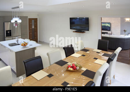 Kitchen dining room in a newly refurbished house showing living room beyond, TVs in both rooms, a plastic cover over the table Stock Photo