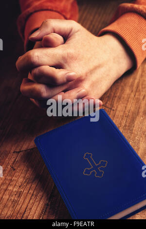 Christian woman praying with hands crossed and Holy Bible by her side on wooden desk in church Stock Photo