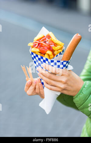 Female hands holding paper cone with a hot sausage and french fries with ketchup Stock Photo