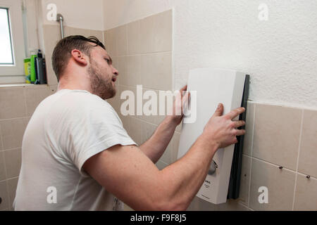 Plumber installs continuous-flow water heater in the bathroom Stock Photo