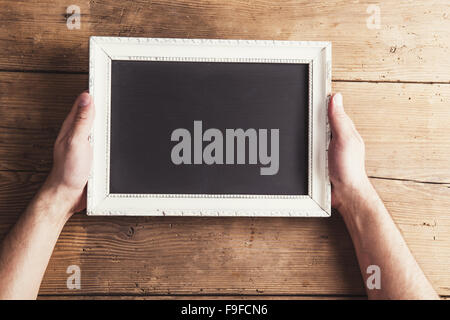 Hands of the father holding white picture frame on wooden floor background. Stock Photo