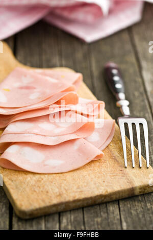 Slices of Sausage Mortadella and fork on cutting board Stock Photo