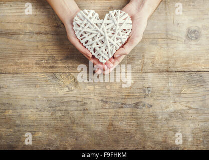 Hands of man and woman holding a heart together. Studio shot on a wooden background, view from above. Stock Photo