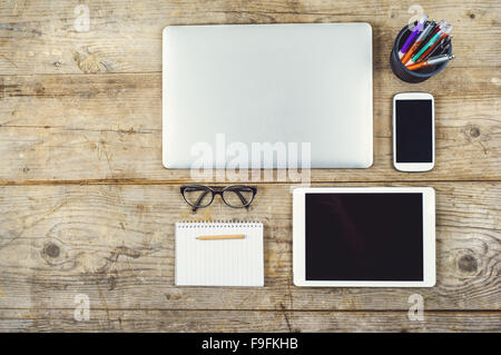 Mix of office supplies and gadgets on a wooden desk background. View from above. Stock Photo