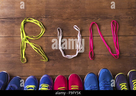 Five pairs of running shoes and shoelaces run sign on a wooden floor background Stock Photo