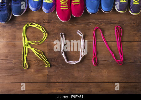 Five pairs of running shoes and shoelaces run sign on a wooden floor background Stock Photo