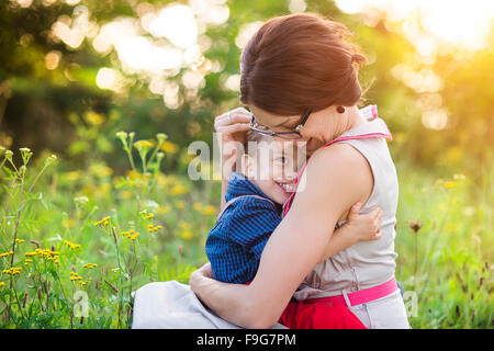 Happy young mother holding her son outside in summer nature Stock Photo