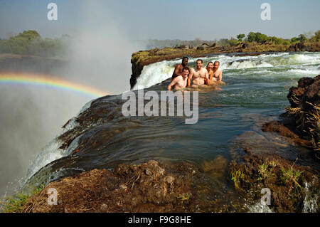 Western tourists with an African guide swim at the edge of the Victoria Falls in Devil's Pool, Zambia Stock Photo