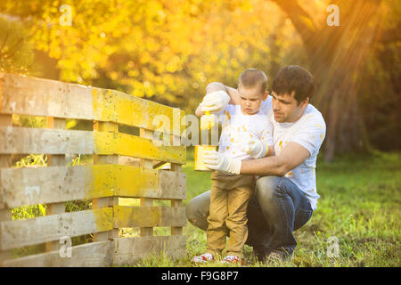 Cute little boy and his father painting wooden fence together on sunny day in nature Stock Photo