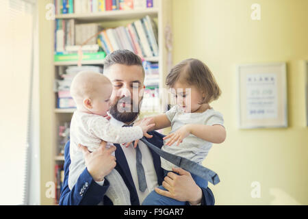 Young father hugging his daughters as he gets home from work Stock Photo