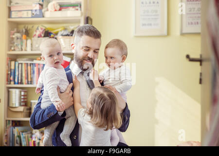 Young father hugging his daughters as he gets home from work Stock Photo